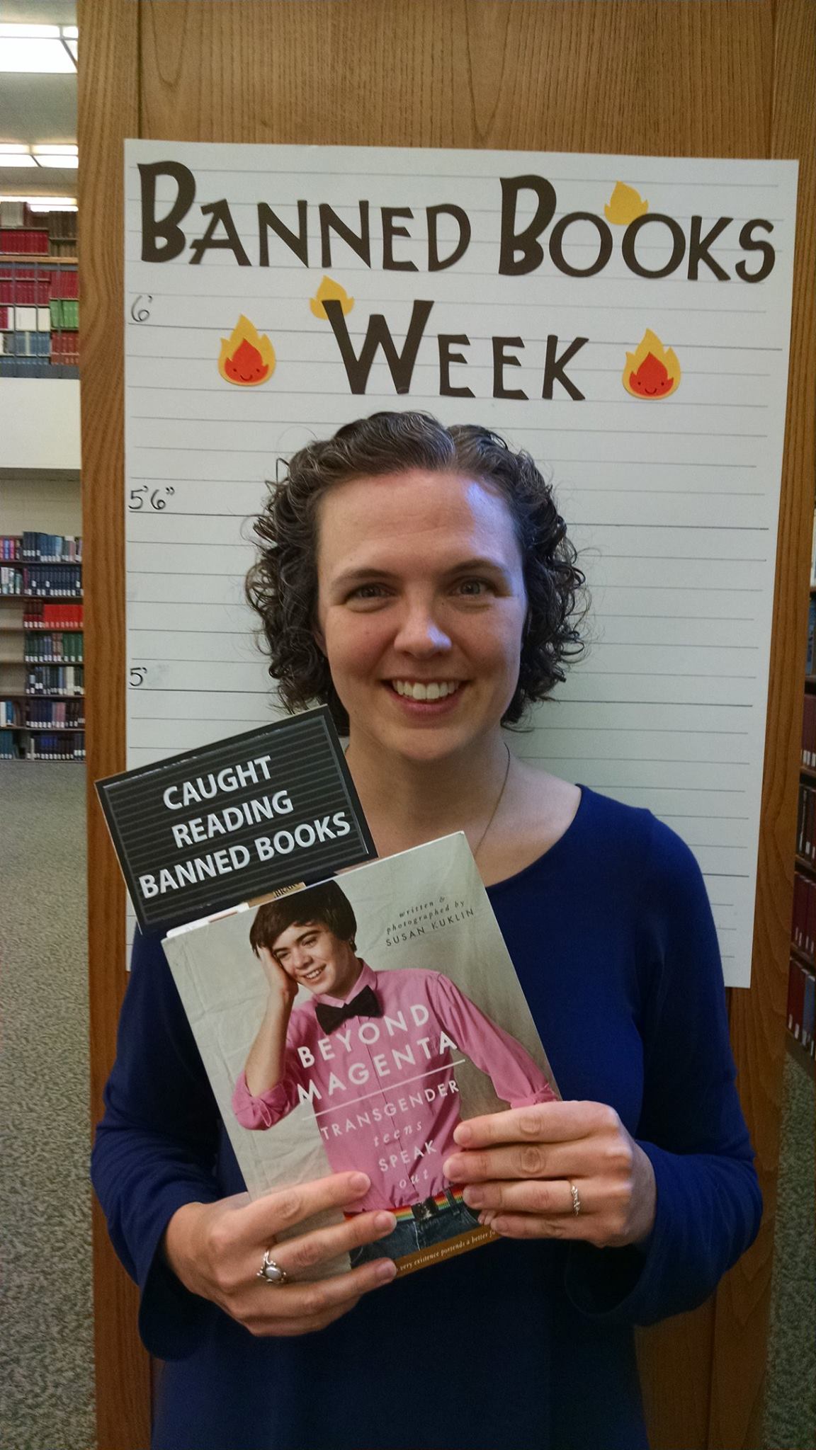 Picture of Mary holding "Beyond Magenta" book in front of a Banned Books Week poster